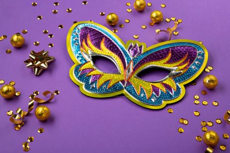 Photo for Mardi Gras masquerade festival carnival mask, sweet chocolate candies, gold beads and golden confetti on purple background. Holiday party invitation, greeting card concept, cope space - Royalty Free Image