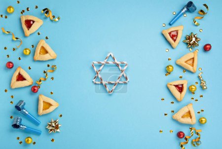 Foto de Purim celebration jewish carnival holiday concept. Tasty hamantaschen cookies, Carnival noisemakers, sweet candies and party decor on blue background. Top view, flat lay, copy space. - Imagen libre de derechos