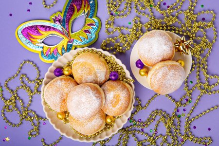 Photo for Mardi Gras King Cake doughnuts or donuts, masquerade festival carnival mask, gold beads and golden, green confetti on purple background. Holiday party invitation, greeting card concept. - Royalty Free Image