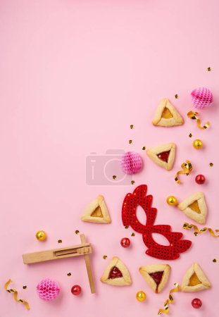 Téléchargez les photos : Purim celebration jewish carnival holiday concept. Tasty hamantaschen cookies, Triangular pastry, red carnival mask, noisemaker, sweet candies and party decor on pink background, Top view, copy space - en image libre de droit