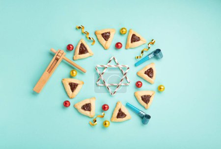 Photo for Purim celebration jewish holiday concept. Tasty hamantaschen cookies, Triangular pastry, Carnival mask, noisemaker, sweet candies and festive party decor on mint green background, Top view, copy space - Royalty Free Image