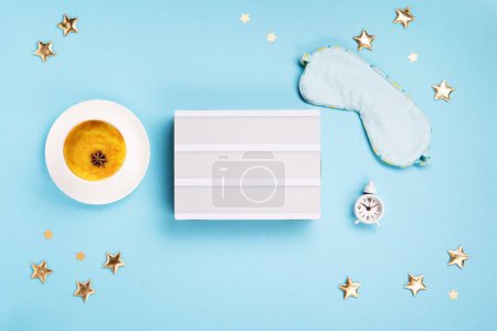 Photo for World Sleep day observed on March. Quality of sleep, good night, insomnia, relaxation concept. Sleeping mask, Turmeric golden milk latte and white alarm clock on blue background. Flat lay, top view - Royalty Free Image
