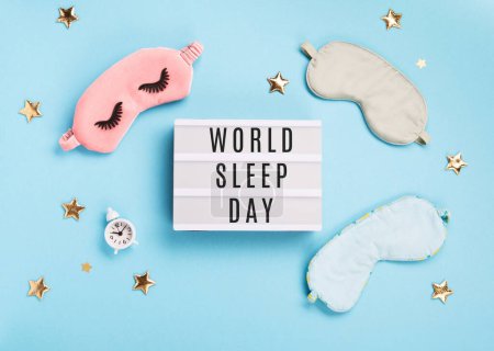 Téléchargez les photos : World Sleep day observed on March. Quality of sleep, good night, insomnia, relaxation concept. Sleeping masks, golden stars and white alarm clock on blue background. Flat lay, top view - en image libre de droit