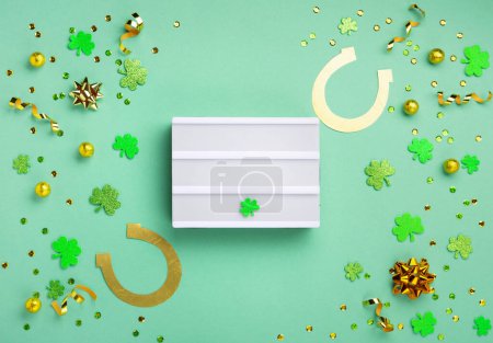 Téléchargez les photos : St. Patrick's Day celebration Concept. Greeting card with traditional symbols - Golden horseshoe, gold coins and clover leaves, green shamrocks on green mint background. Top view, copy space. - en image libre de droit