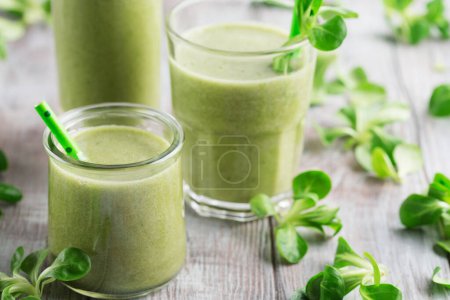 Photo for Fresh detox green drinks in glasses with spinach all around them on white rustic wood table, healthy eating concept - Royalty Free Image