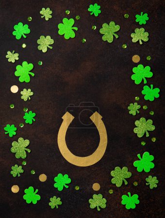 Téléchargez les photos : St. Patrick's Day celebration Concept. Greeting card with traditional symbols - Golden horseshoe, gold coins and clover leaves, green shamrocks on dark brown wooden background. Top view, copy space. - en image libre de droit