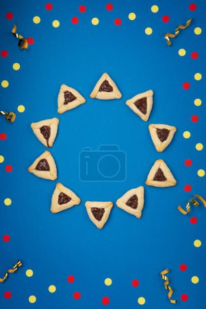 Photo for Homemade Purim hamantaschen cookies, Triangular pastry, Carnival mask, noisemaker, sweet candies and festive party decor on dark blue background, Top view. Purim celebration jewish holiday concept. - Royalty Free Image