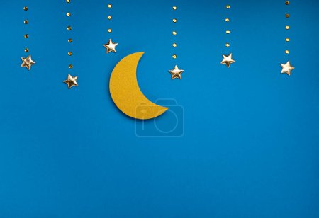 Téléchargez les photos : Ramadan Kareem holiday concept. Golden crescent moon and stars on blue background. Traditional Muslim Iftar. Top view, copy space. - en image libre de droit