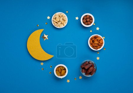 Photo for Ramadan Kareem concept. Date fruits, cashew nuts, almonds and crescent moon on blue background. Traditional Muslim Iftar Food. Top view, copy space. - Royalty Free Image