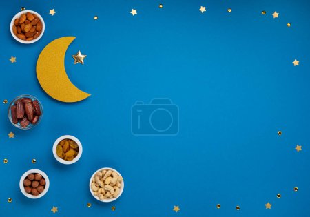Photo for Ramadan Kareem concept. Date fruits, cashew nuts, almonds and crescent moon on blue background. Traditional Muslim Iftar Food. Top view, copy space. - Royalty Free Image