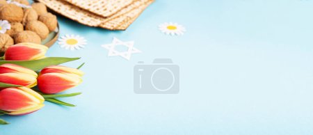 Téléchargez les photos : Jewish holiday Passover greeting card concept with matzah, nuts and tulip flowers on blue background. Seder Pesach spring holiday background, copy space. - en image libre de droit