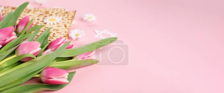 Photo for Jewish holiday Passover greeting card concept with matzah, nuts, tulip and daisy flowers on pink table. Seder Pesach spring holiday background, copy space. - Royalty Free Image