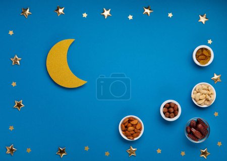 Foto de Ramadan Kareem concept. Date fruits, cashew nuts, almonds and crescent moon on blue background. Traditional Muslim Iftar Food. Top view, copy space. - Imagen libre de derechos