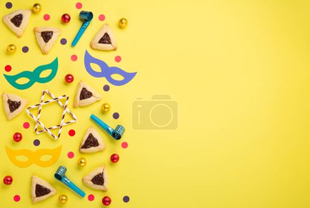 Téléchargez les photos : Biscuits Pourim hamantaschen maison, pâtisserie triangulaire, masque de carnaval, bruyant, bonbons sucrés et décor de fête sur fond jaune, vue sur le dessus. Pourim célébration juive concept de vacances. - en image libre de droit