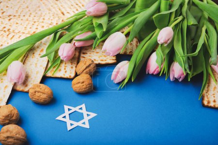 Photo for Jewish holiday Passover greeting card concept with matzah, nuts, tulip flowers on blue table Seder Pesach spring holiday background, top view, copy space. - Royalty Free Image