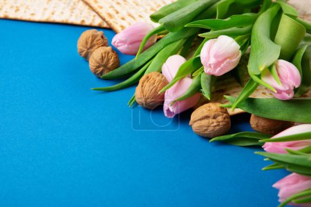 Foto de Judía fiesta Pascua tarjeta de felicitación concepto con matzá, nueces, flores de tulipán en la mesa azul Seder Pesaj primavera vacaciones fondo, vista superior, espacio de copia. - Imagen libre de derechos
