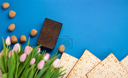 Téléchargez les photos : Jewish holiday Passover greeting card concept with matzah, nuts, tulip flowers on blue table Seder Pesach spring holiday background, top view, copy space. - en image libre de droit
