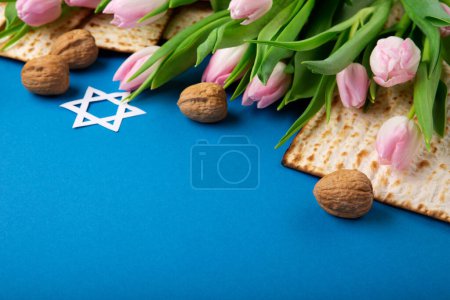 Photo for Jewish holiday Passover greeting card concept with matzah, nuts, tulip flowers on blue table Seder Pesach spring holiday background, top view, copy space. - Royalty Free Image
