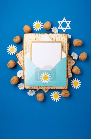 Téléchargez les photos : Jewish holiday Passover greeting card concept with matzah, nuts, spring flowers on blue table. Seder Pesach spring holiday background, top view, copy space. - en image libre de droit
