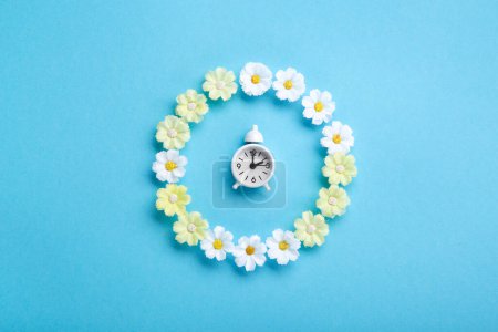 Téléchargez les photos : White alarm clock and Daisy Flowers on blue background. Spring forward, Time Change, Daylight Saving Time Ends, Changing the time on the watch to spring time, Summer back concept. - en image libre de droit