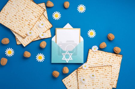 Téléchargez les photos : Jewish holiday Passover greeting card concept with matzah, nuts, spring flowers on blue table. Seder Pesach spring holiday background, top view, copy space. - en image libre de droit