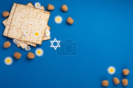 Jewish holiday Passover greeting card concept with matzah, nuts, spring flowers on blue table. Seder Pesach spring holiday background, top view, copy space.