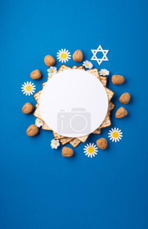 Jewish holiday Passover greeting card concept with matzah, nuts, spring flowers on blue table. Seder Pesach spring holiday background, top view, copy space.