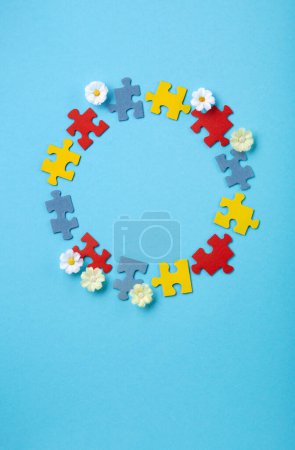 Téléchargez les photos : Journée mondiale de sensibilisation à l'autisme ou concept de mois. Design créatif pour le 2 avril. Puzzle de couleur, symbole de sensibilisation aux troubles du spectre autistique et aux fleurs de marguerite sur fond bleu. Vue du dessus, espace de copie. - en image libre de droit