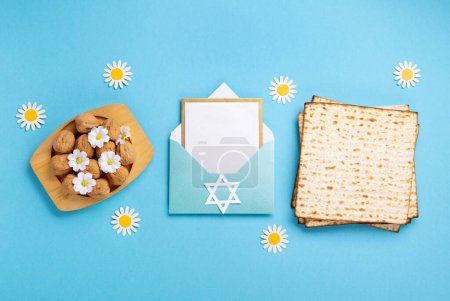 Téléchargez les photos : Jewish holiday Passover greeting card concept with matzah, walnuts, daisy flowers and empty envelope on blue table. Seder Pesach spring holiday background, top view, copy space. - en image libre de droit