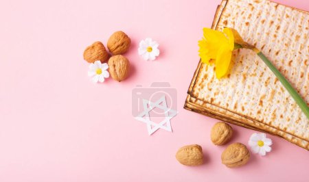 Téléchargez les photos : Jewish holiday Passover greeting card concept with matzah, nuts, spring daisy flowers on pink table. Seder Pesach spring holiday background, copy space. - en image libre de droit