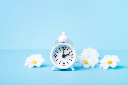 Photo for White alarm clock and Daisy Flowers on blue background. Spring forward, Time Change, Daylight Saving Time Ends, Changing the time on the watch to spring time, Summer back concept. - Royalty Free Image