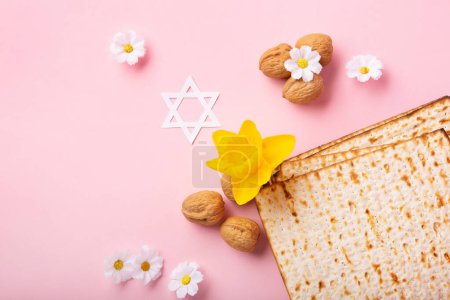 Téléchargez les photos : Jewish holiday Passover greeting card concept with matzah, Star of David, spring yellow daffodil, daisy flowers, walnuts on pink table. Seder Pesach spring holiday background, copy space. - en image libre de droit