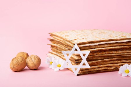 Téléchargez les photos : Jewish holiday Passover greeting card concept with matzah, Star of David, spring daisy flowers, walnuts on pink table. Seder Pesach spring holiday background, copy space. - en image libre de droit