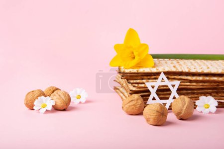 Foto de Jewish holiday Passover greeting card concept with matzah, Star of David, spring yellow daffodil, daisy flowers, walnuts on pink table. Seder Pesach spring holiday background, copy space. - Imagen libre de derechos