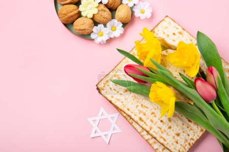 Téléchargez les photos : Jewish holiday Passover greeting card concept with matzah, Star of David, spring yellow daffodil, tulips, daisy flowers, walnuts on pink table. Seder Pesach spring holiday background, copy space. - en image libre de droit