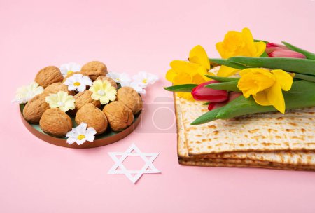 Téléchargez les photos : Jewish holiday Passover greeting card concept with matzah, nuts, spring daisy flowers on pink table. Seder Pesach spring holiday background, copy space. - en image libre de droit