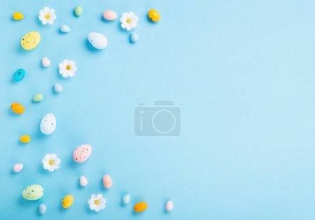 Téléchargez les photos : Sweet Colorful Easter Eggs and white daisy flowers on pastel blue background. Happy Easter greeting card concept. Flat lay, top view, copy space. - en image libre de droit