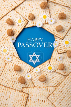 Foto de Jewish holiday Passover greeting card concept with matzah, nuts, spring flowers on blue table. Seder Pesach spring holiday background, top view, copy space. - Imagen libre de derechos