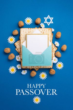 Téléchargez les photos : Jewish holiday Passover greeting card concept with matzah, walnuts, daisy flowers and empty envelope on blue table. Seder Pesach spring holiday background, top view, copy space. - en image libre de droit