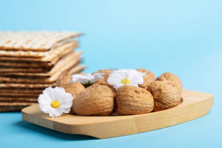 Téléchargez les photos : Jewish holiday Passover greeting card concept with matzah, nuts, spring daisy flowers on blue table. Seder Pesach spring holiday background, copy space. - en image libre de droit