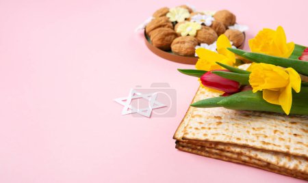 Photo for Jewish holiday Passover greeting card concept with matzah, Star of David, spring yellow daffodil, tulips, daisy flowers, walnuts on pink table. Seder Pesach spring holiday background, copy space. - Royalty Free Image