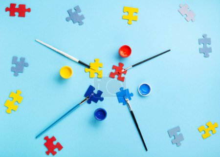 Photo for World Autism Awareness Day or month concept. Creative design for April 2. White puzzles, symbol of awareness for autism spectrum disorder and colorful paints on blue background. Top view, copy space. - Royalty Free Image