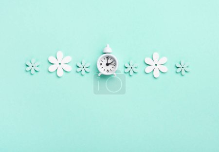 Téléchargez les photos : White alarm clock and Daisy Flowers on blue mint background. Spring forward, Time Change, Daylight Saving Time Ends, Changing the time on the watch to spring time, Summer back concept. - en image libre de droit