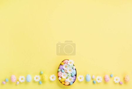 Foto de Dulce colorido huevos de Pascua y flores de margarita blanca primavera sobre fondo amarillo pastel. Feliz Pascua concepto de tarjeta de felicitación. Plano, vista superior, espacio para copiar. - Imagen libre de derechos