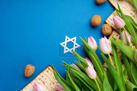 Photo for Jewish holiday Passover greeting card concept with matzah, nuts, tulip flowers on blue table. Seder Pesach spring holiday background, top view, copy space. - Royalty Free Image