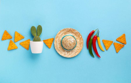 Téléchargez les photos : Fête d'arrière-plan mexicain avec des copeaux de nachos mexicains traditionnels, piment, cactus et chapeau de sombrero sur fond bleu. Cinco de Mayo (Cinquième mai) concept de célébration. Vue du dessus, espace de copie. - en image libre de droit