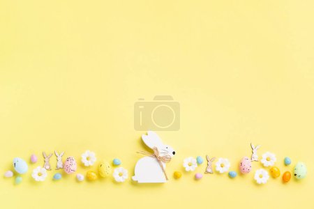 Foto de Conejo de Pascua de madera blanca, huevos de Pascua de colores dulces, flores de margarita sobre fondo amarillo pastel. Feliz Pascua concepto de tarjeta de felicitación, espacio de copia. - Imagen libre de derechos