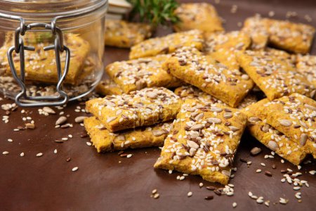 Gluten free Homemade Crackers and rosemary on brown background. Healthy eating, ancient grain food, dieting, balanced food concept. Cereals gluten-free, millet, quinoa, flax seeds, sunflower seeds.