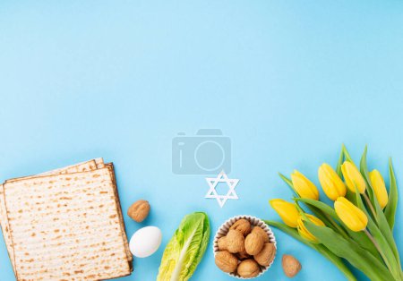Téléchargez les photos : Carte de vœux de Pâques juive concept avec matzah matzoh (pain de vacances juif), noix, fleurs de tulipes jaunes sur table bleue. Seder Pessah printemps fond de vacances, vue sur le dessus. - en image libre de droit