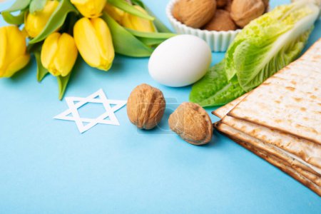 Photo for Jewish holiday Passover greeting card concept with matzah matzoh (jewish holiday bread), walnuts, yellow tulip flowers on blue table. Seder Pesach spring holiday background, copy space. - Royalty Free Image